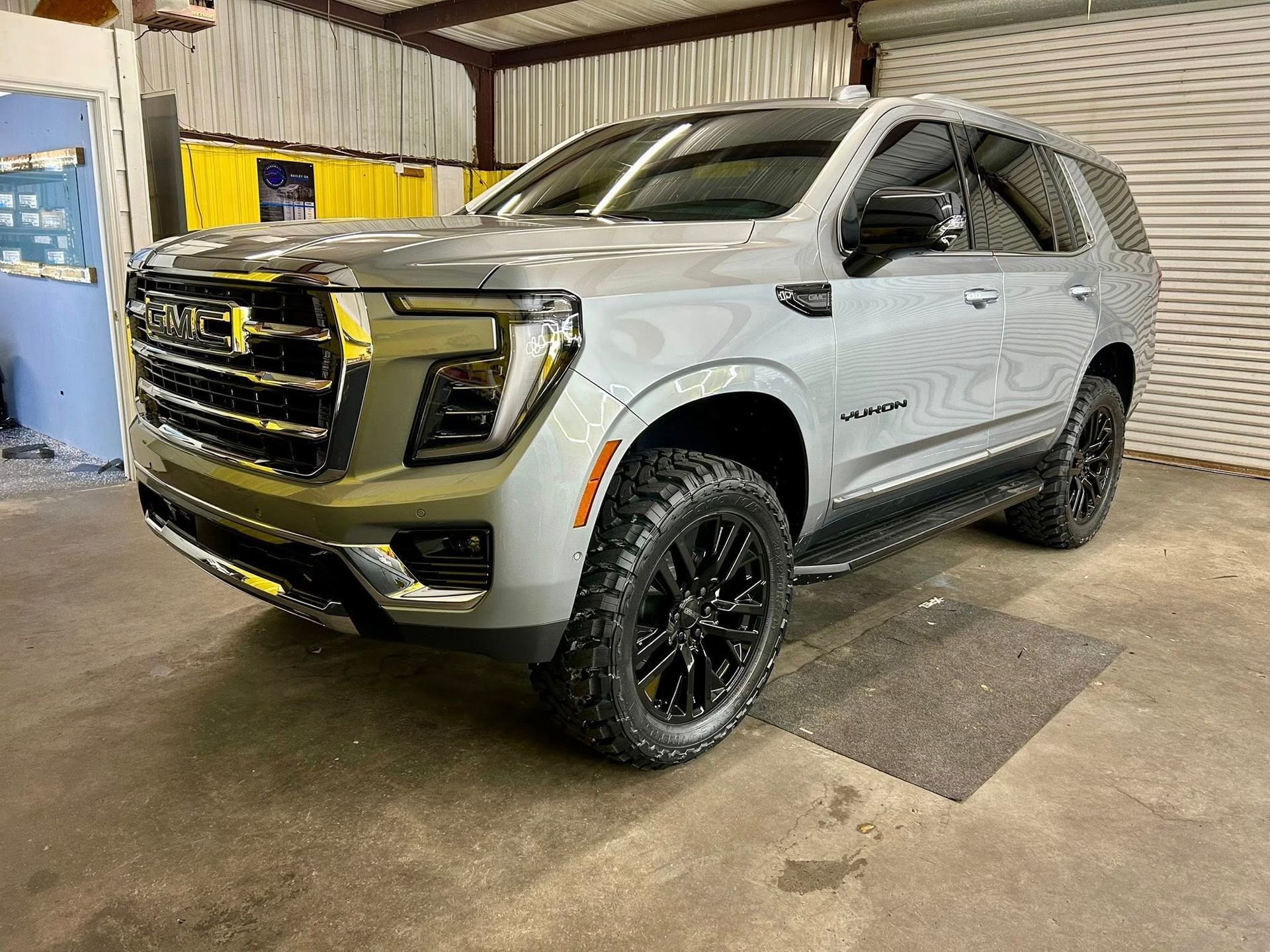 Silver GMC Yukon SUV parked inside a garage, black wheels and tinted windows.