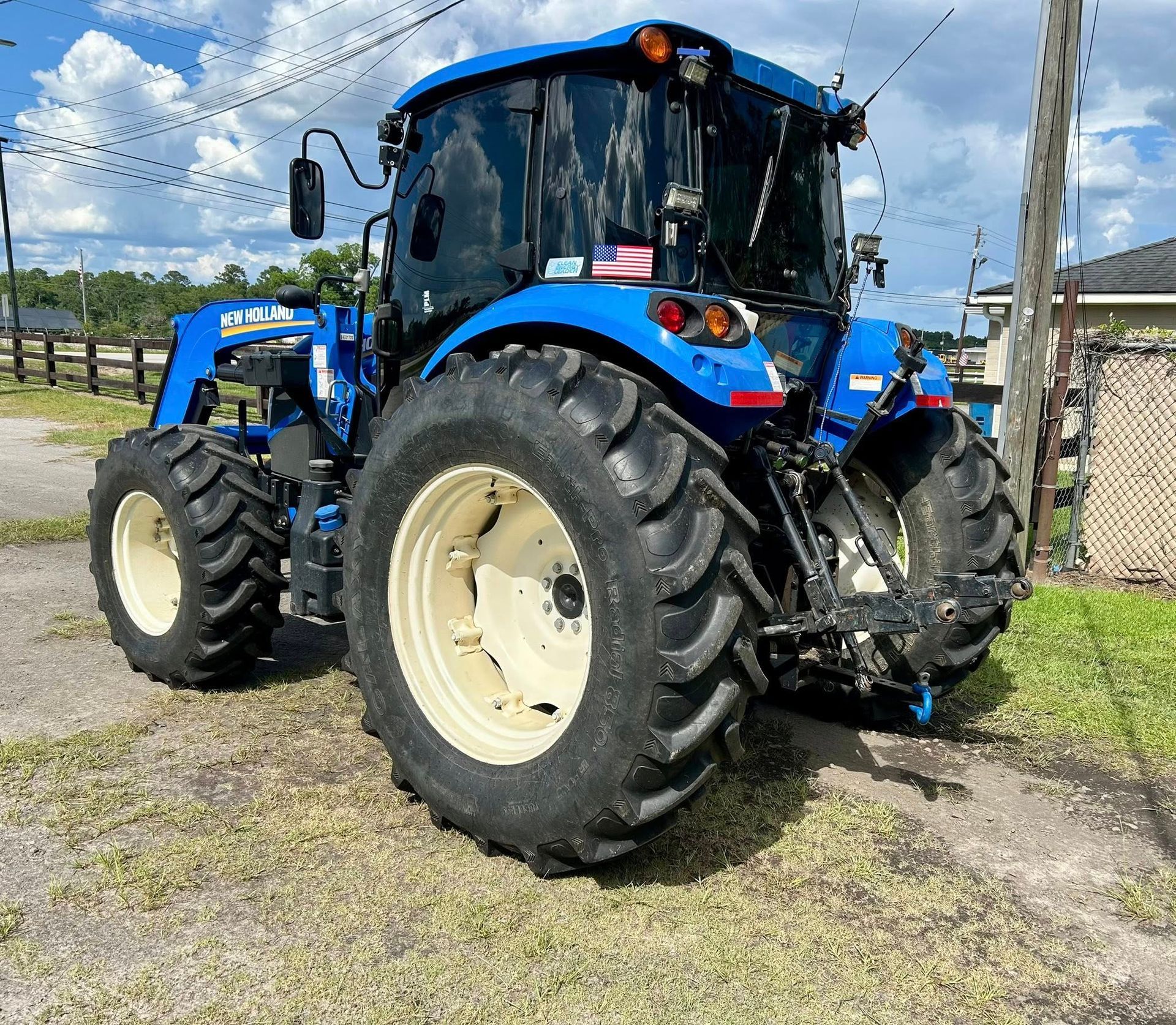 Blue tractor with large tires parked on a grassy area, a sunny day.
