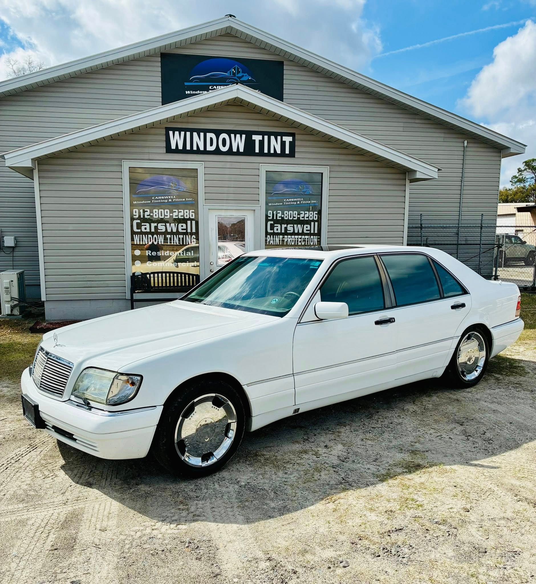 White Mercedes-Benz sedan parked in front of a window tint shop; sunny day.