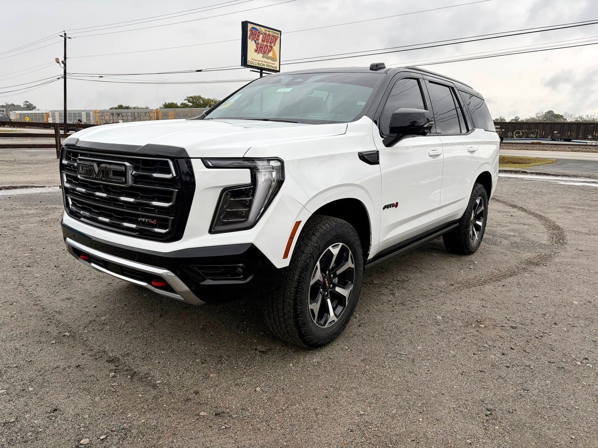 White GMC Yukon SUV parked on gravel, black accents, cloudy sky.