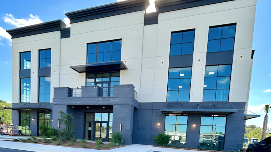 Modern two-story building with large windows and a dark gray facade. Blue sky in the background.