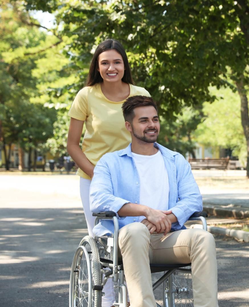 Woman pushing a man in a wheelchair along a paved path, both smiling.