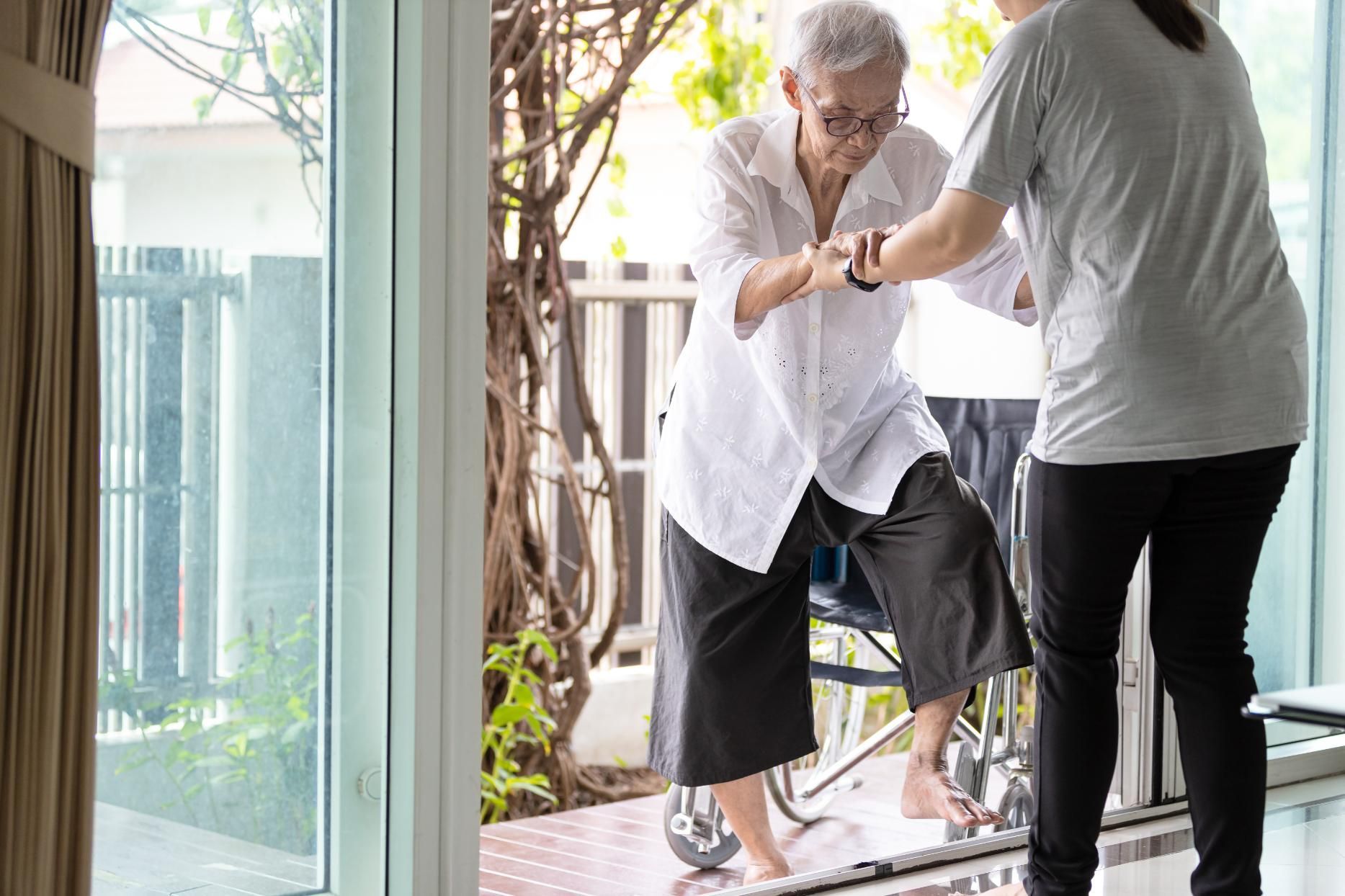 Woman assisting an elderly person out of a wheelchair onto a balcony.