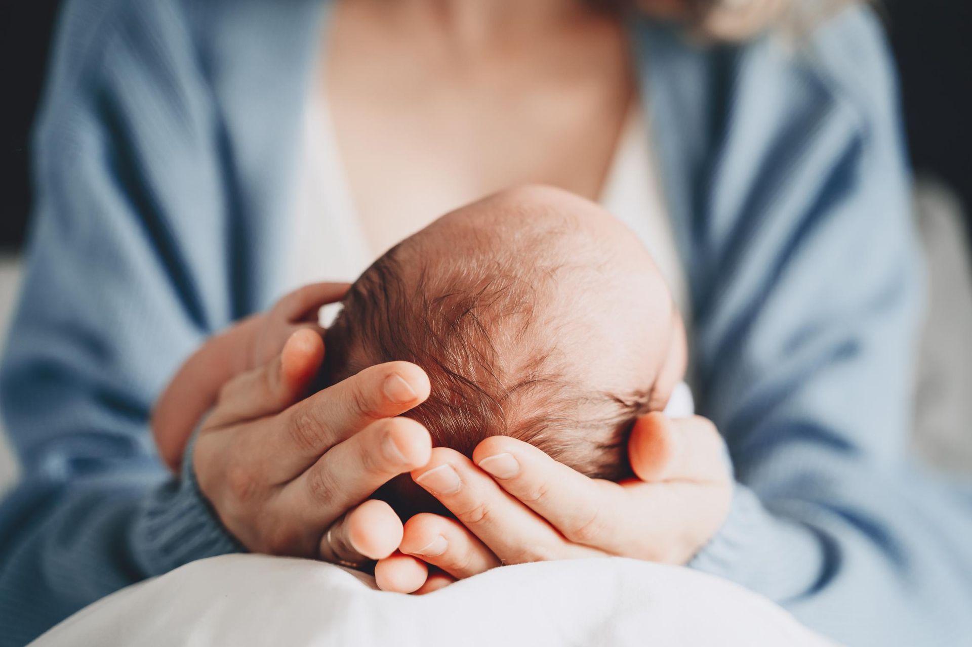 Person cradling a newborn baby's head with both hands; baby's head visible, hands in focus.