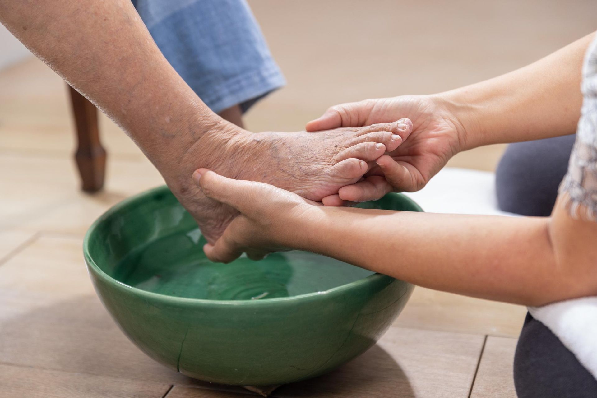 Hands washing an elderly person's foot in a green bowl of water.
