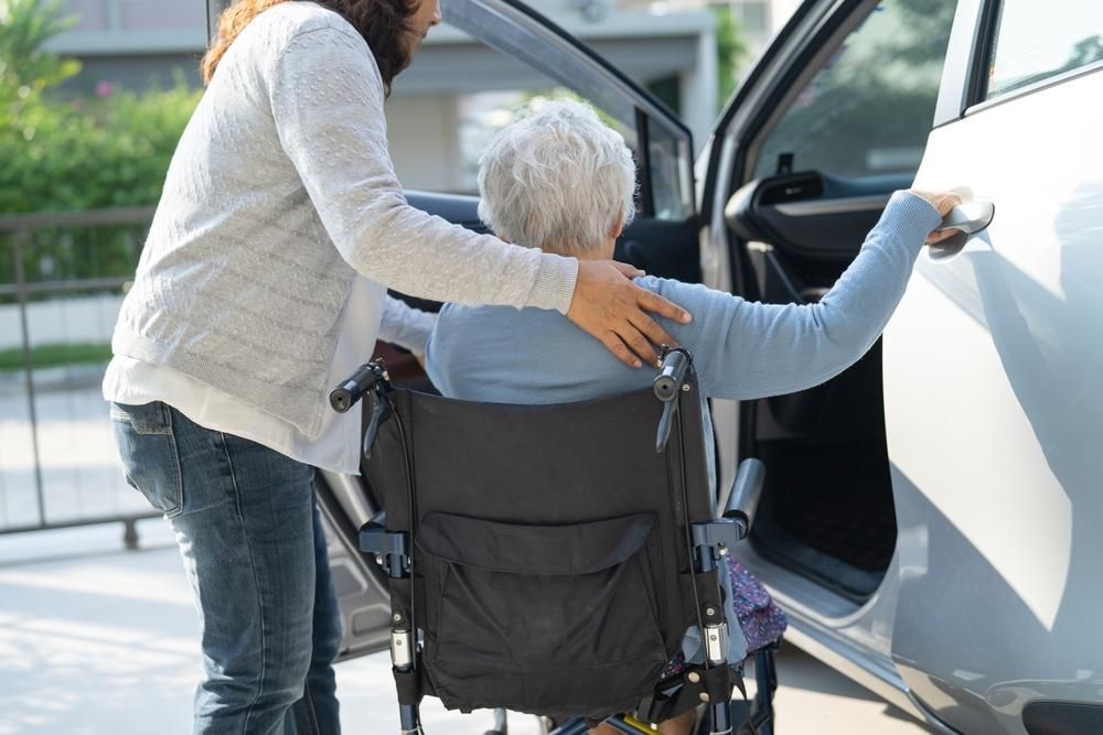 Person assisting a person in a wheelchair into a car.