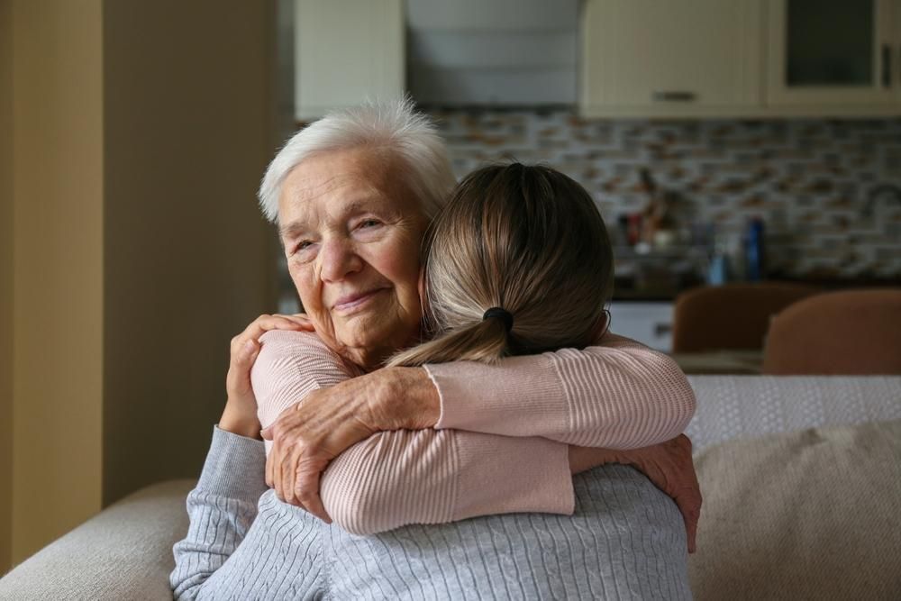 Woman embraces elderly woman, both smiling, indoors.