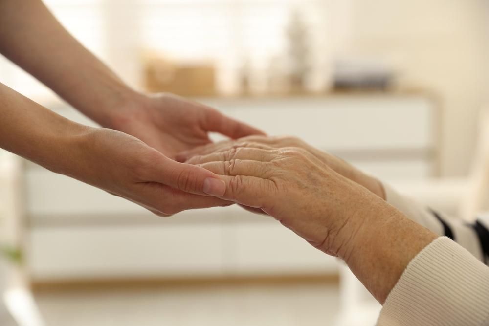 Young hands gently holding an older person's hands indoors, showing care and support.