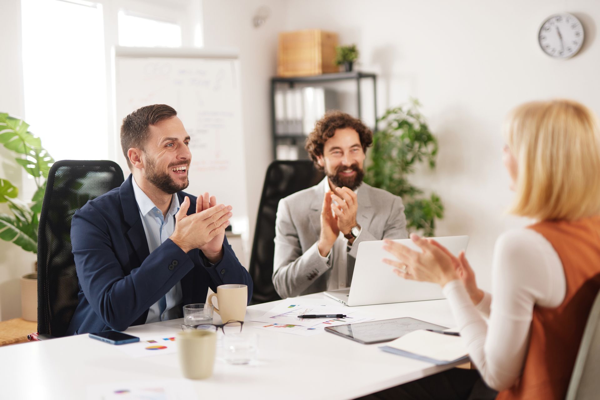 Three people in business attire applaud around a table in an office.
