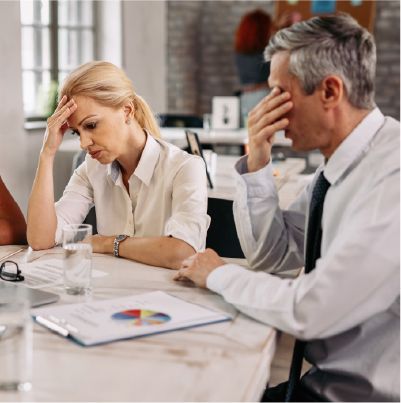 Woman and man looking stressed in a meeting, papers and a graph on the table.