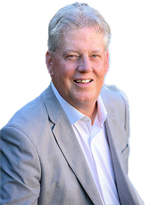 Man in light gray suit smiles, leaning forward. White shirt, natural background.