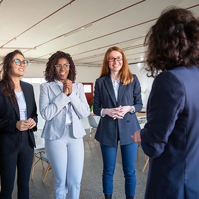 Four people in suits listening to a person. They appear happy and engaged. Indoors, office-like setting.