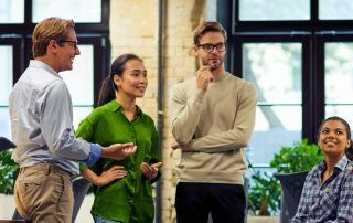 Four people in a room are talking; one man gestures, two women and one man listen.