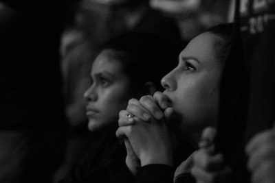 Two women, side profiles, looking up, clasped hands in front of faces, possibly in prayer.