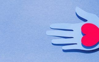 Blue paper cutout hand holding a red heart on a blue background.