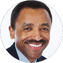 Smiling man with mustache in a dark suit, light blue shirt, in a circular frame.