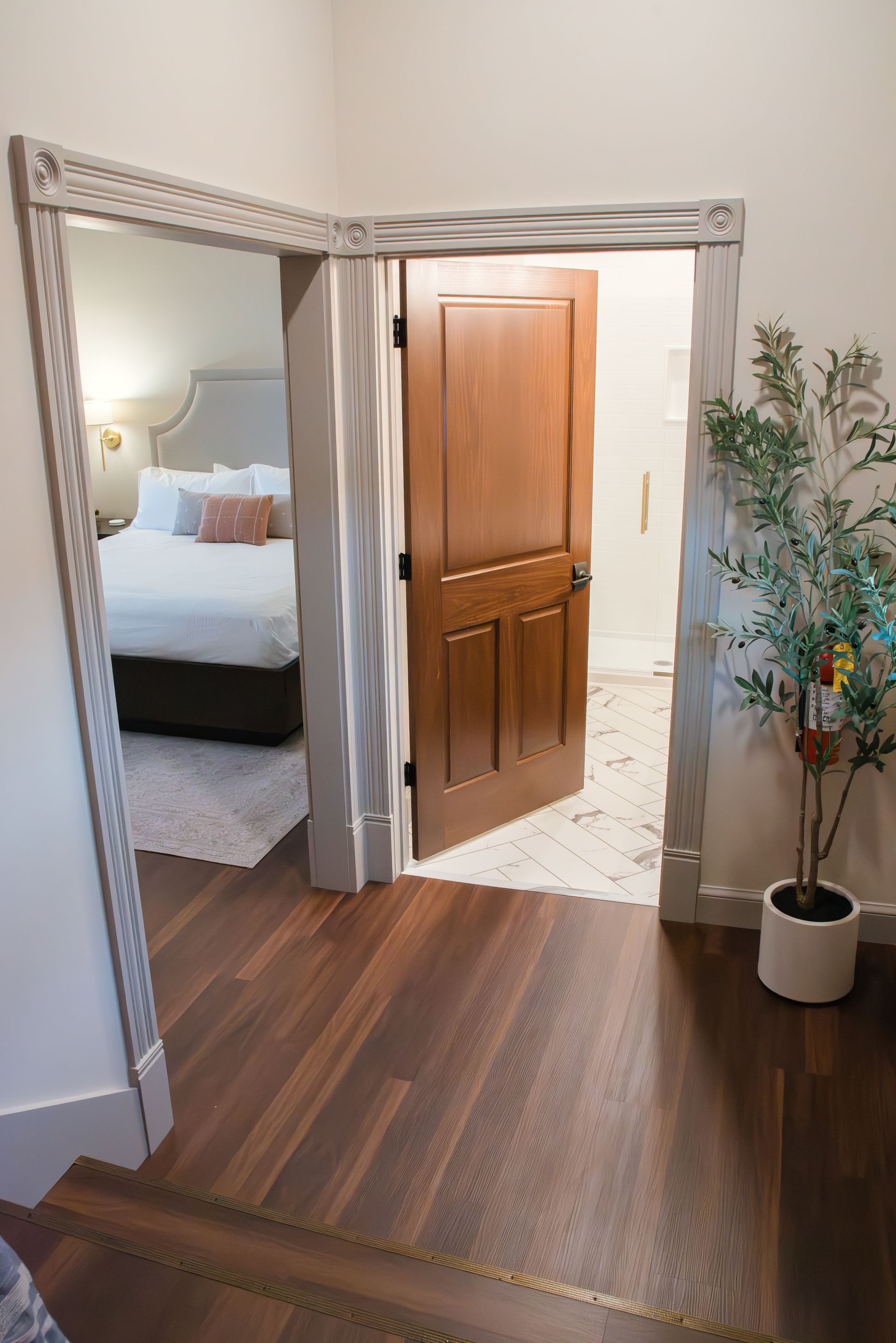 Doorway leads to bedroom and bathroom; wood floors, brown door, neutral colors.