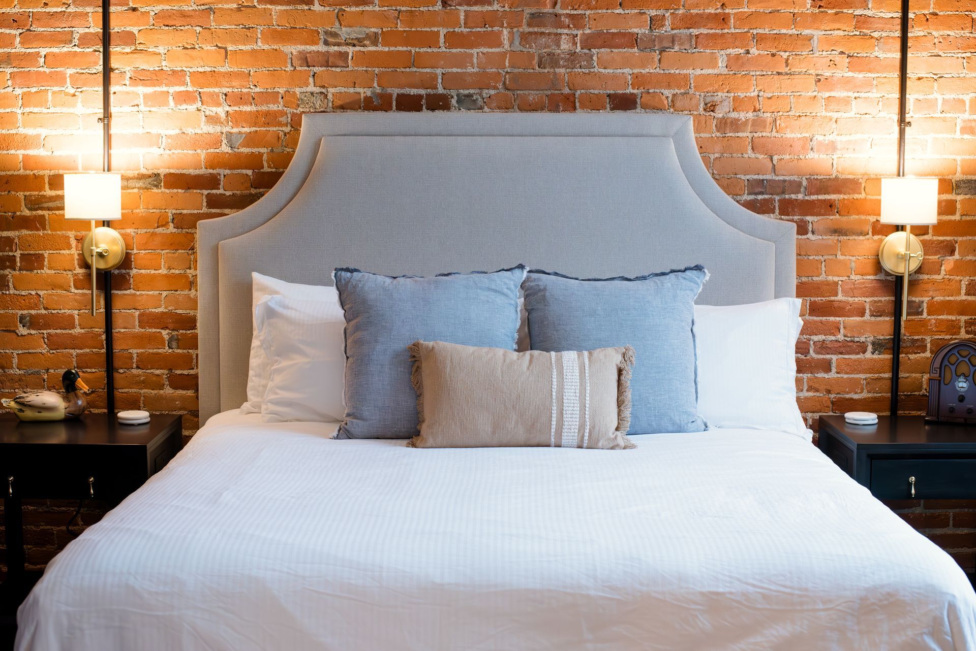 Bed in a room with exposed brick walls, bedside tables, lamps, and decorative pillows.