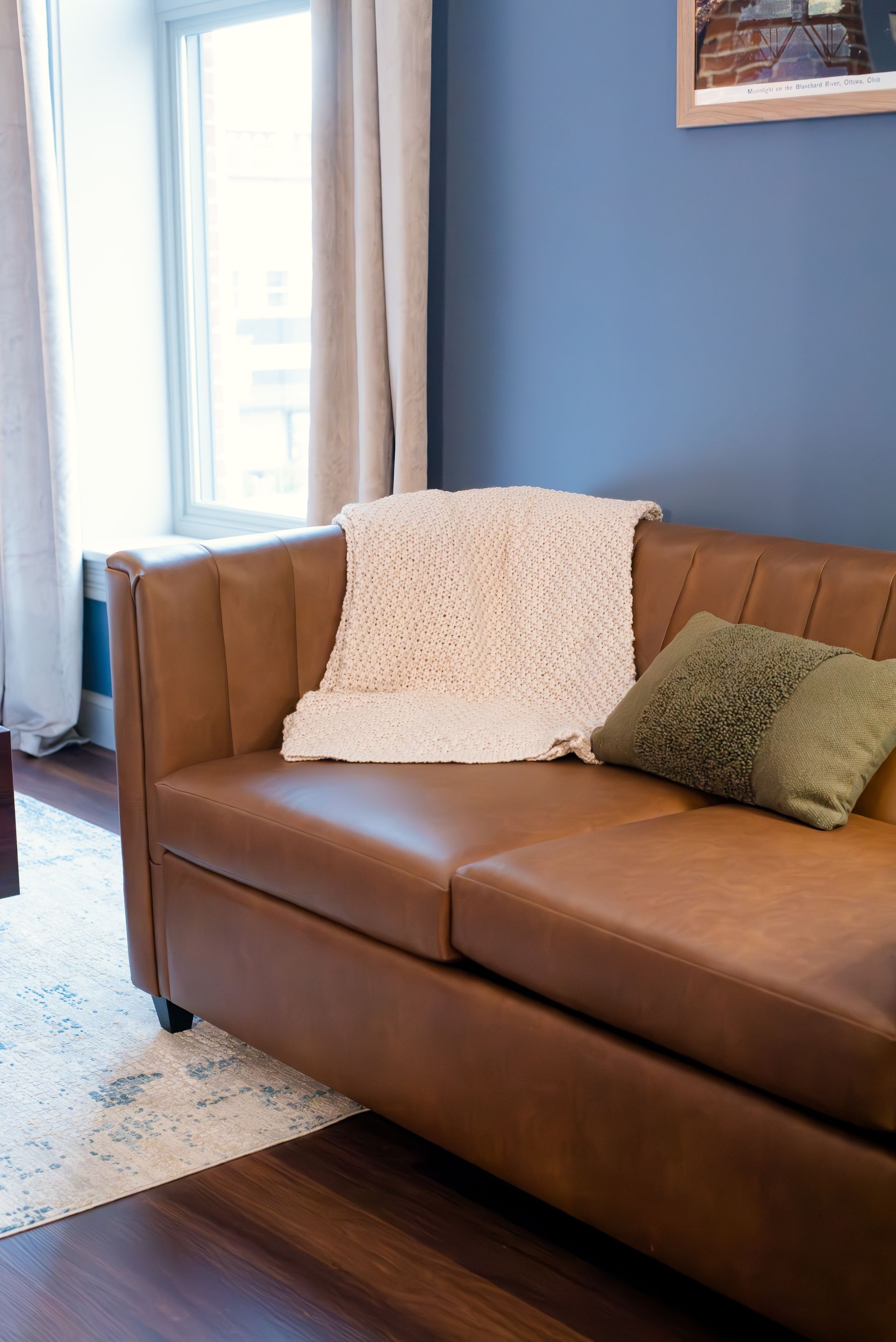 Brown leather sofa with a white blanket and green pillow in a blue-walled room.