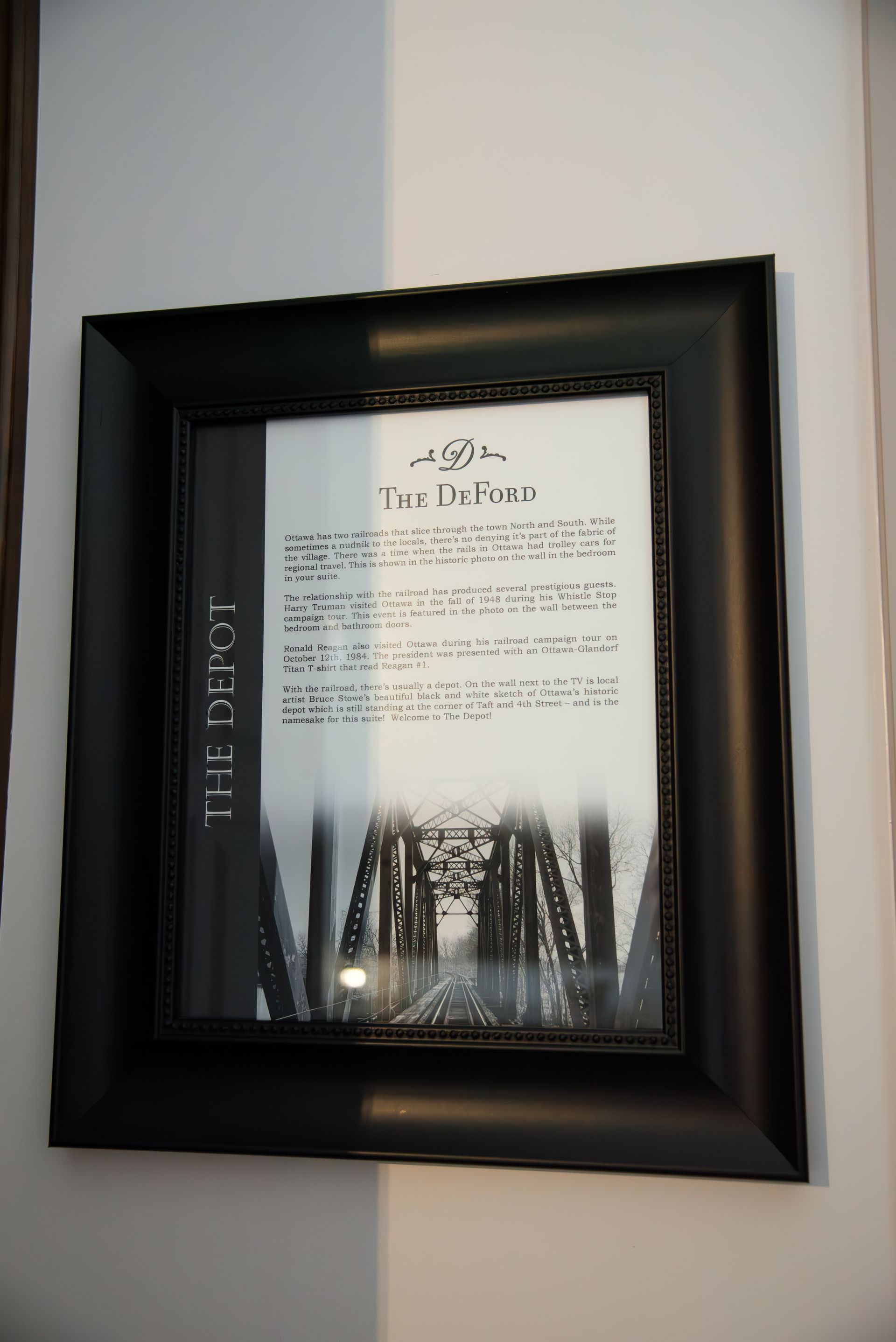 Black framed artwork on a white wall. It has a photo of a bridge with text overlaid.
