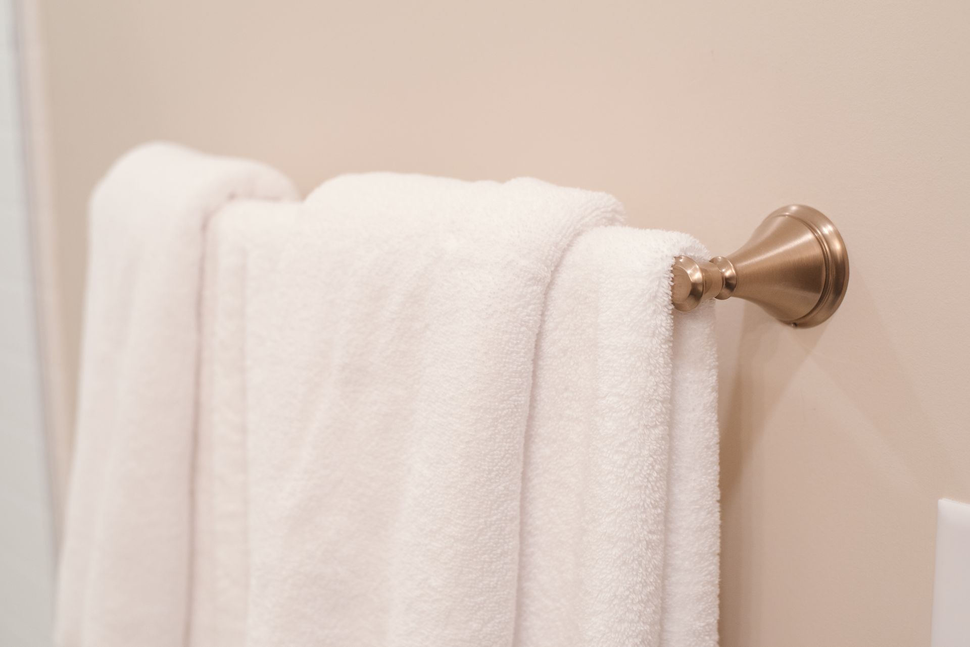 White towel draped on a bronze towel bar against a light beige wall.