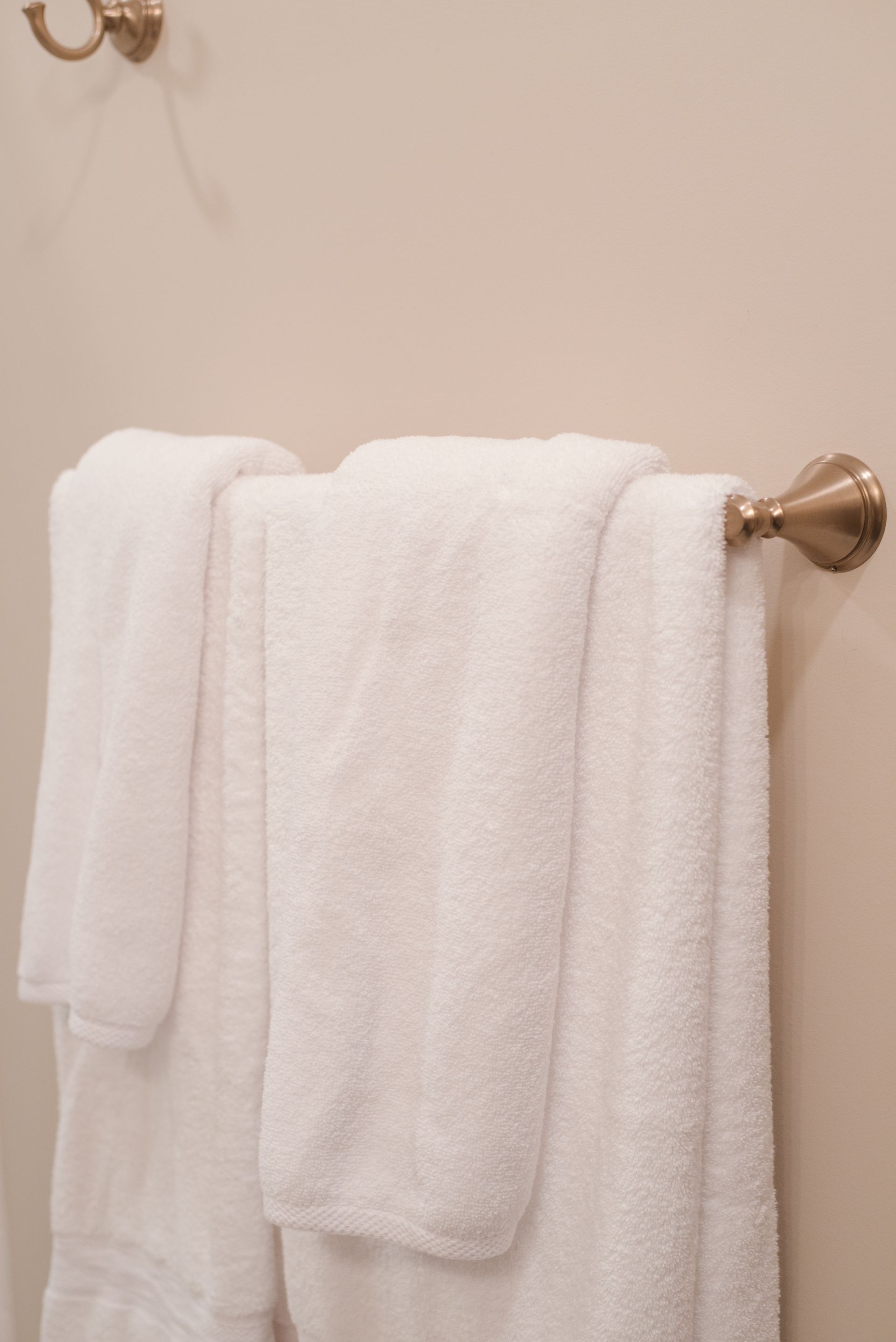 White towels hanging on a brass towel rack in a bathroom.