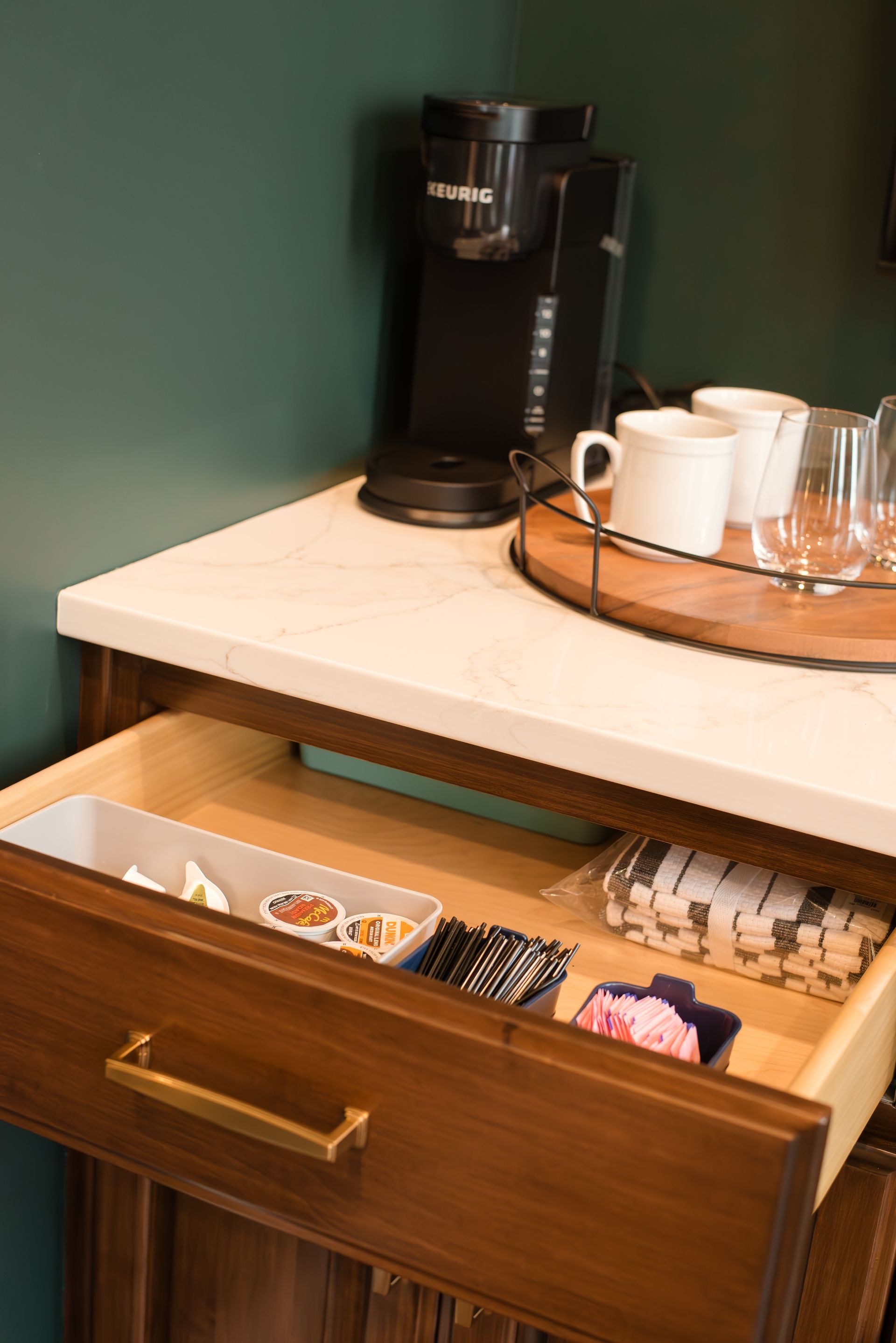 Coffee station with a Keurig machine, mugs, and drawer with supplies.