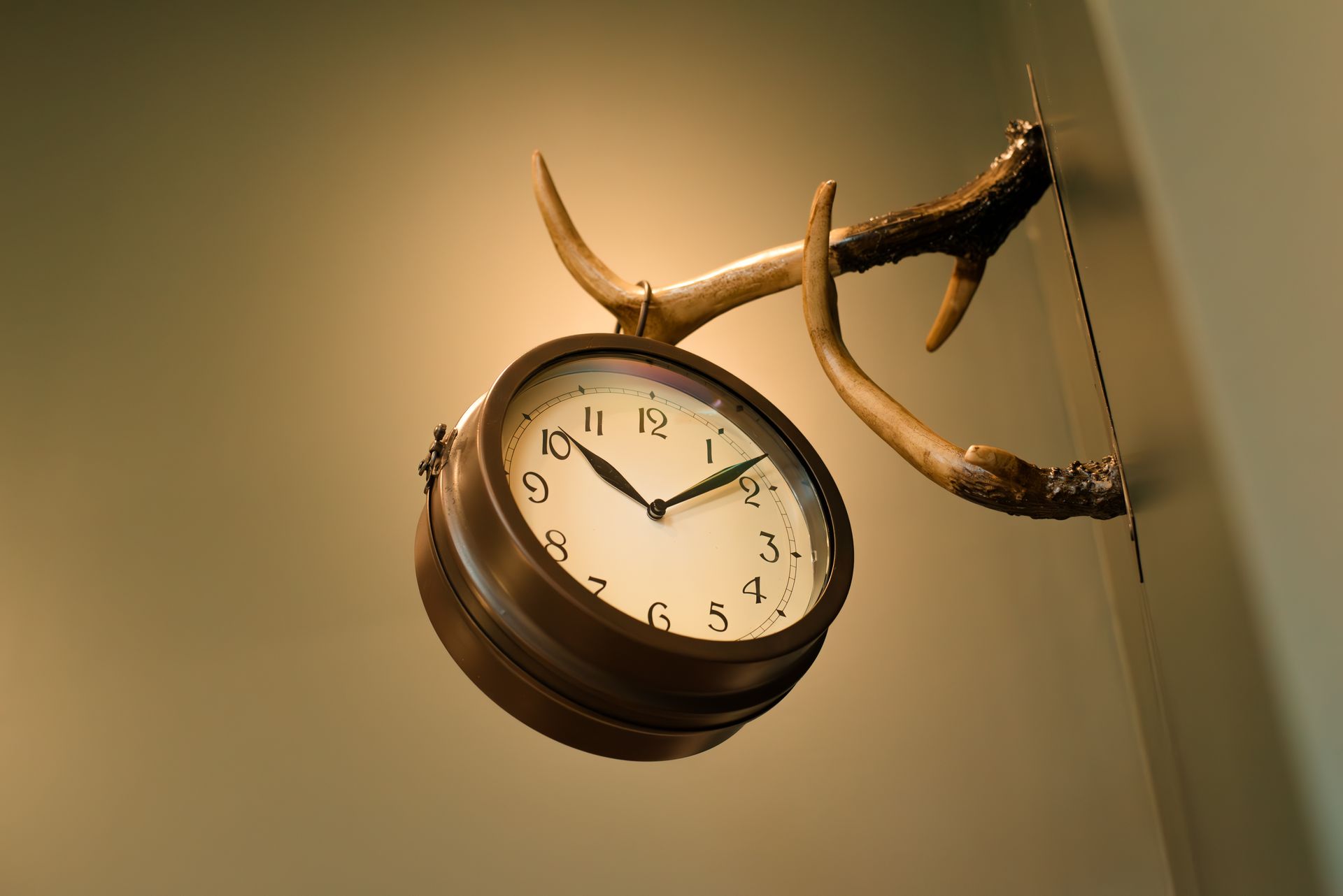 Clock with antlers hanging on a beige wall.