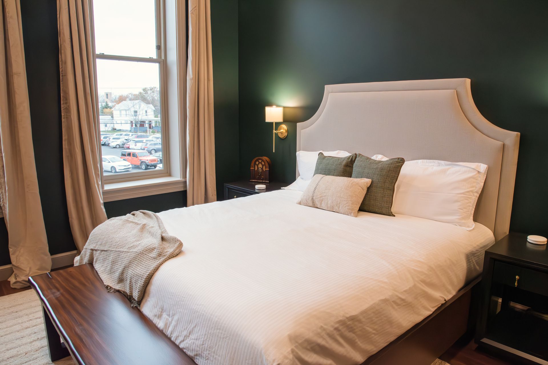 Bedroom with a bed, nightstand, window, dark green walls, and beige curtains.