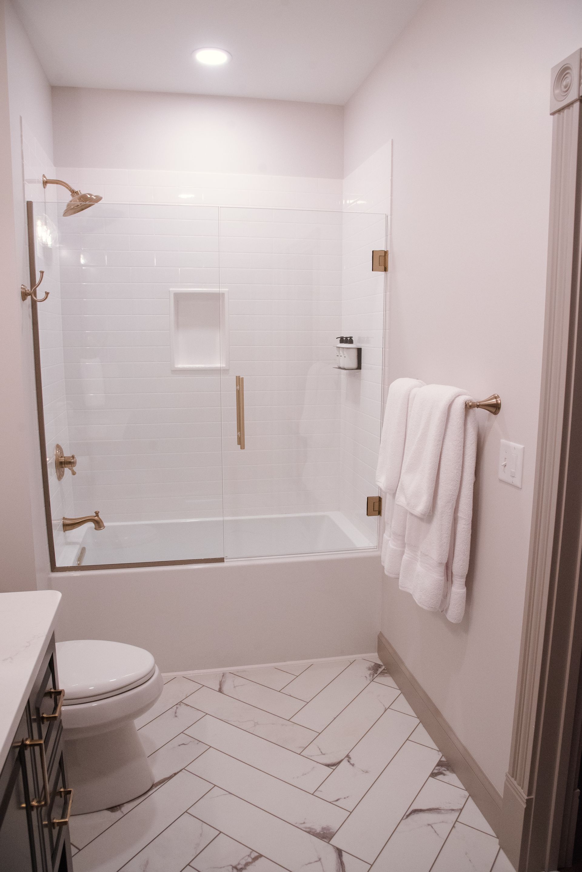 Small modern bathroom with white subway tile, gold fixtures, and white towels.