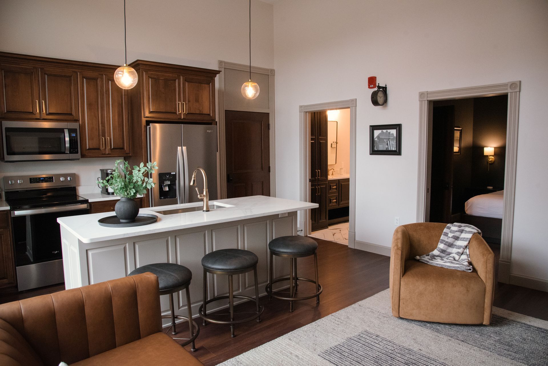 Kitchen/living area with brown cabinets, island with stools, and entry to bedroom/bathroom.