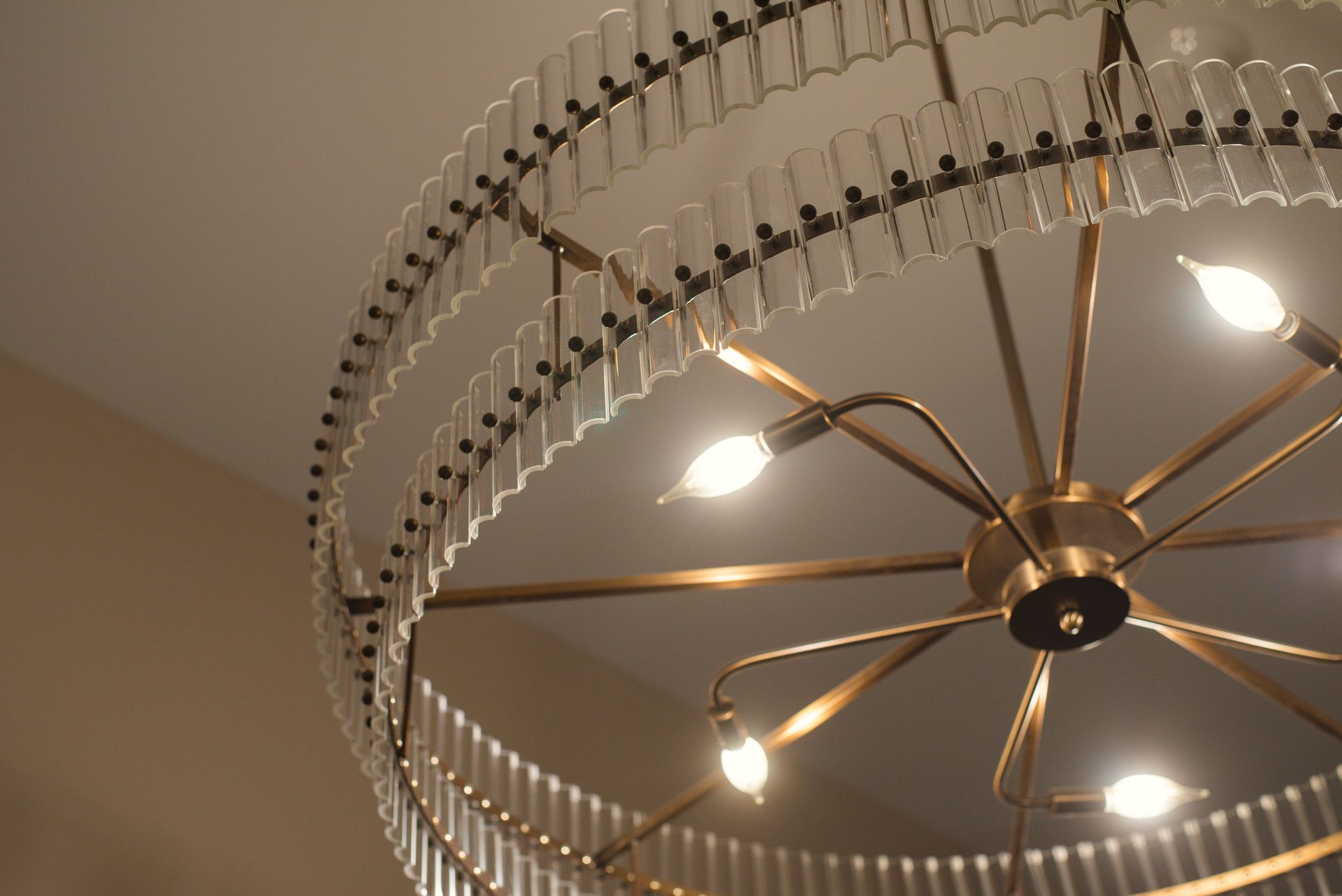 Chandelier with a circular design featuring glass tubes and glowing light bulbs against a cream-colored ceiling.