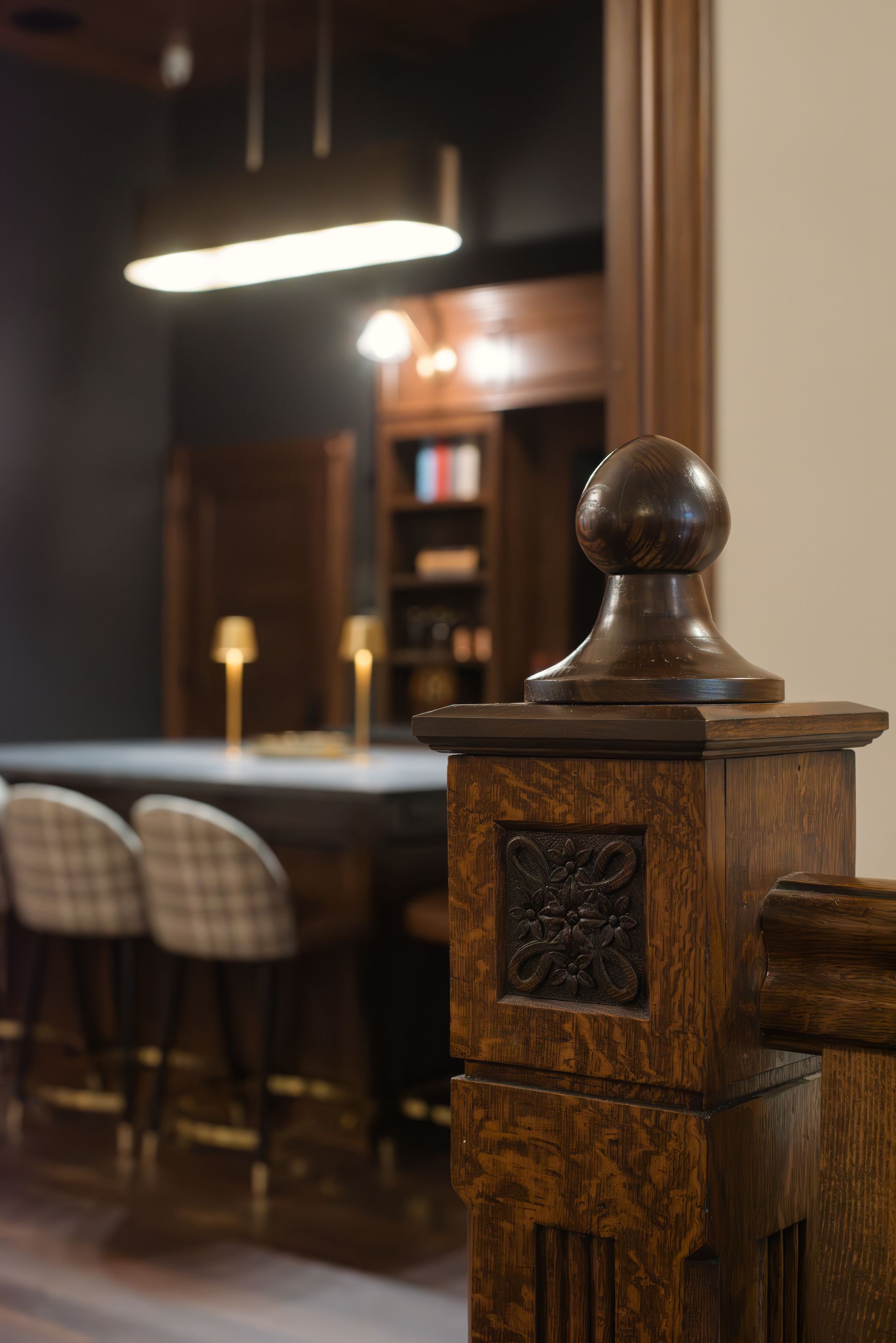 Close-up of a wooden post with a decorative carving, bar in the background with stools and lights.