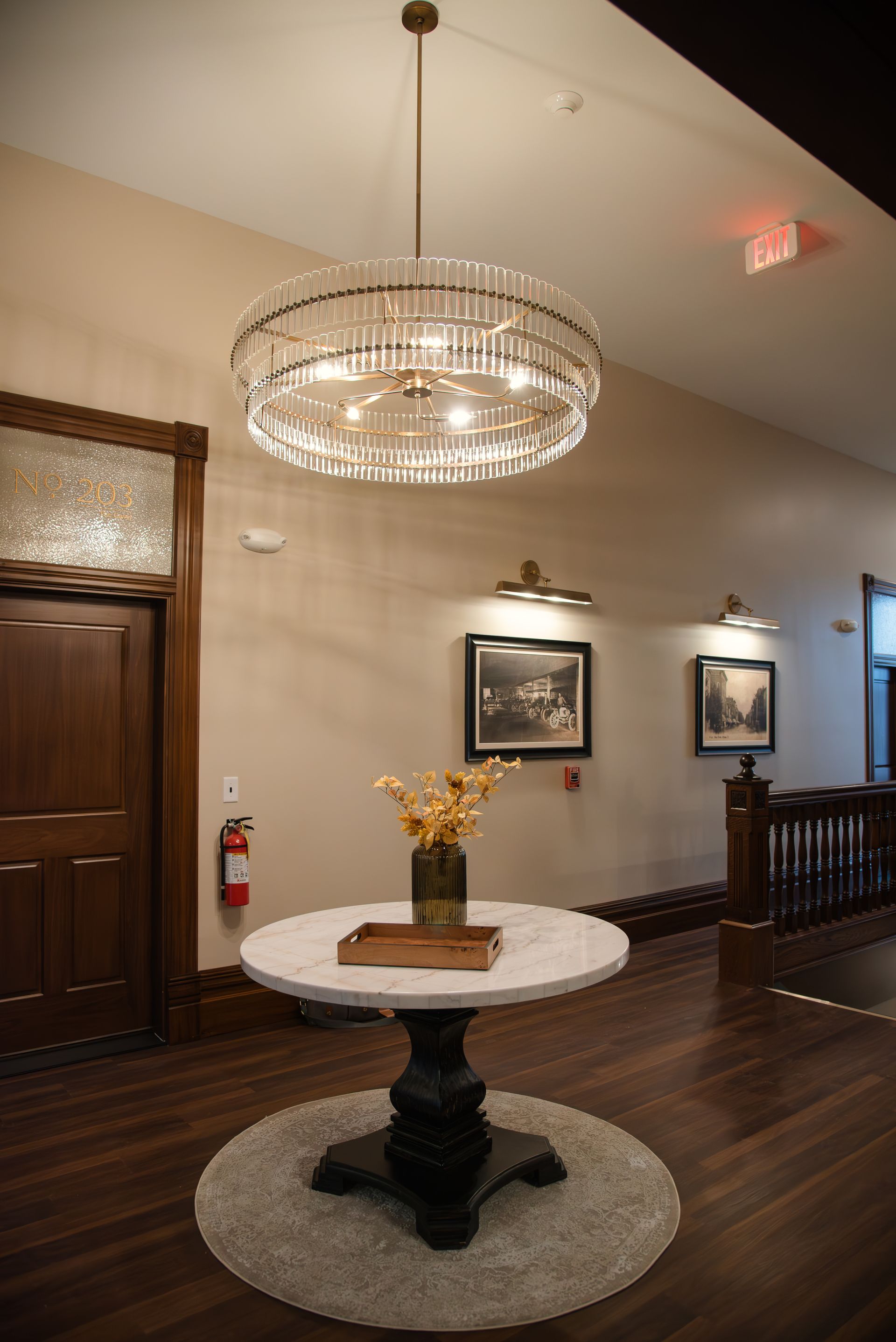 Elegant foyer with a round marble table, chandelier, artwork, and wooden door.