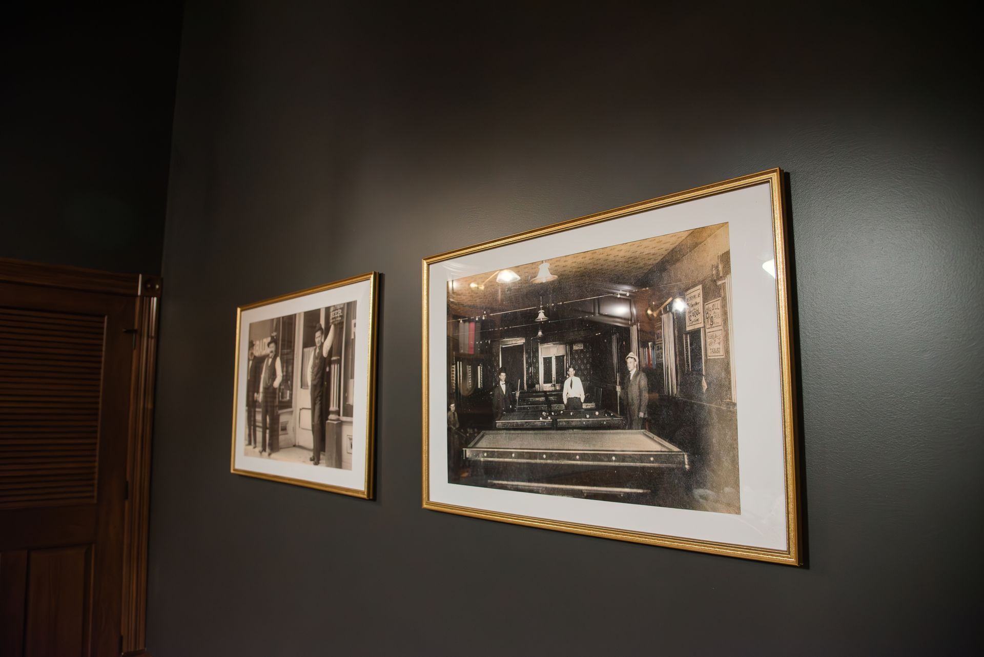 Two framed vintage photos on a dark wall. One depicts a man, the other, a pool hall.