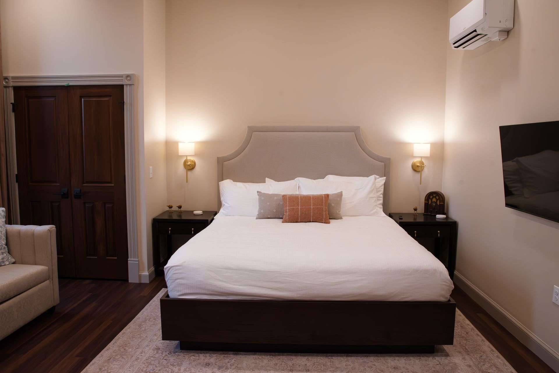 Bedroom with queen bed, nightstands, wall-mounted TV, and cream-colored walls and furniture.