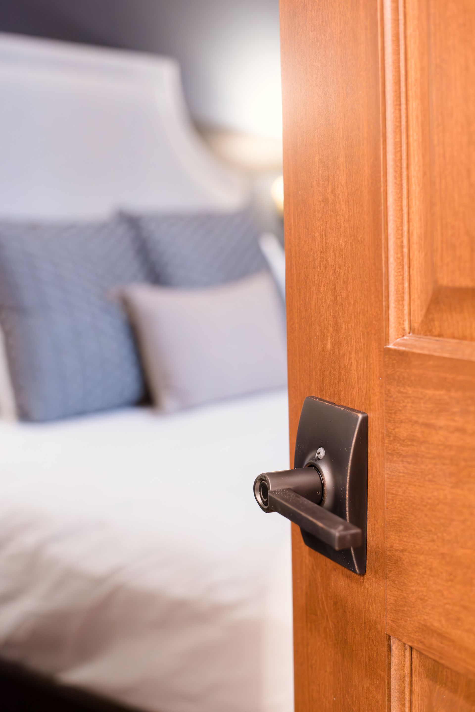 Open wooden door with bronze handle, revealing a bed with pillows.