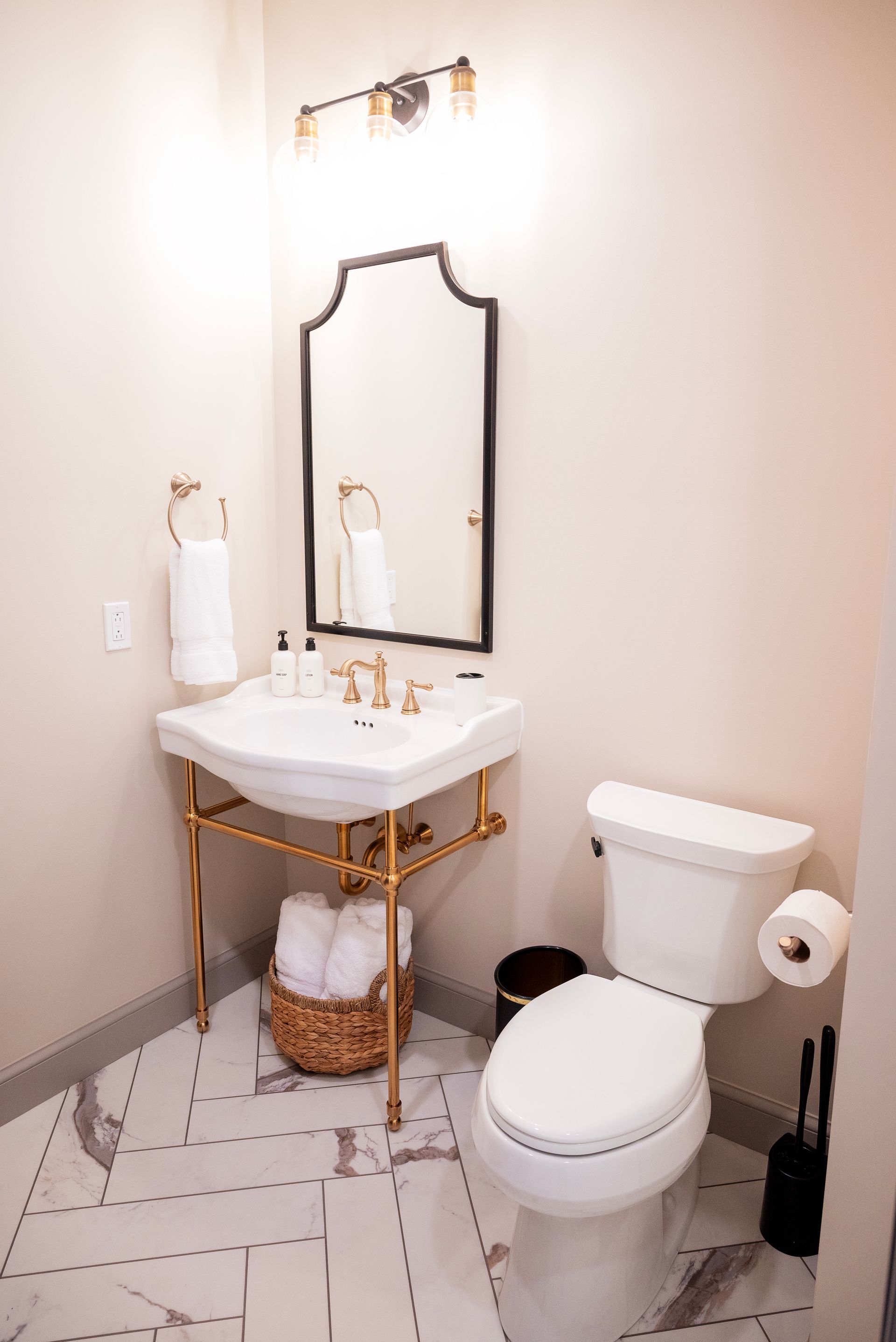 Elegant powder room with gold accents, white sink, black mirror, and marble floors.