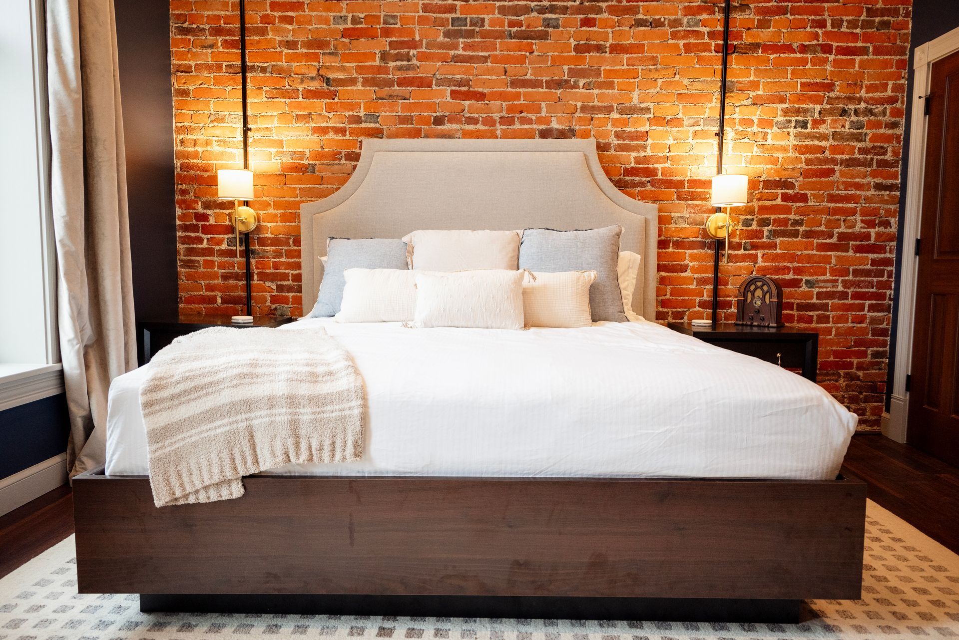 Bedroom with bed against a brick wall, two sconces, and a rug.