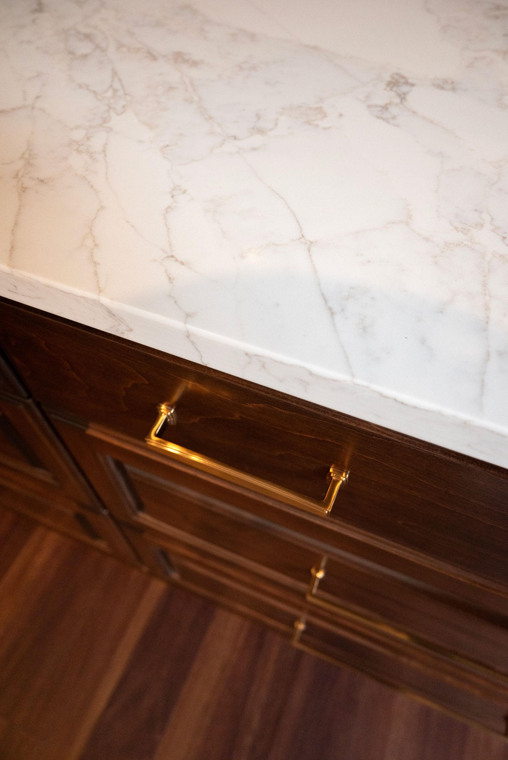 Marble countertop with gold drawer pulls on dark wooden cabinets.
