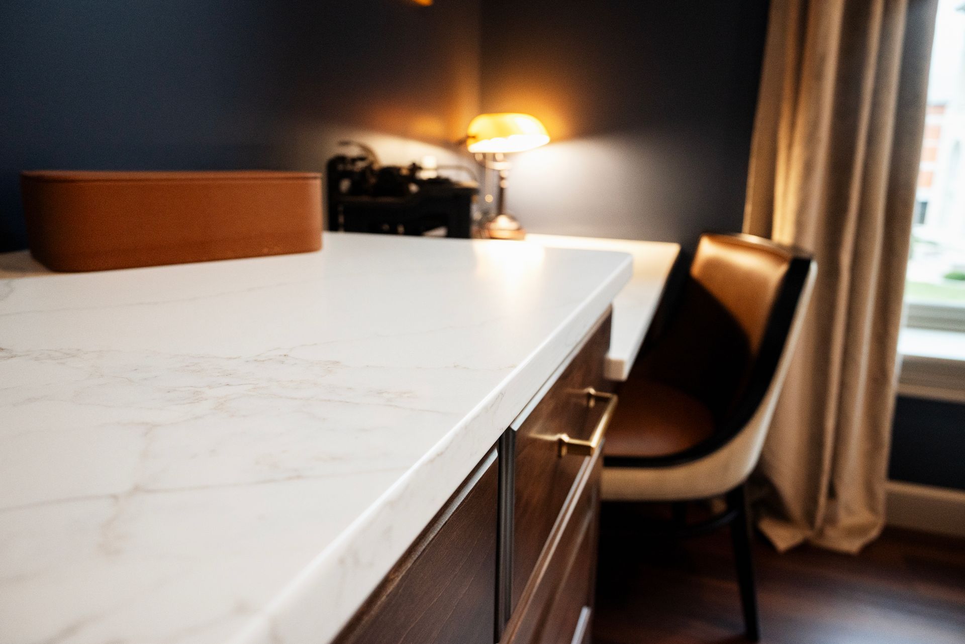 Close-up of a white marble countertop with brown drawers. A brown speaker, lamp, and chair are in the background.