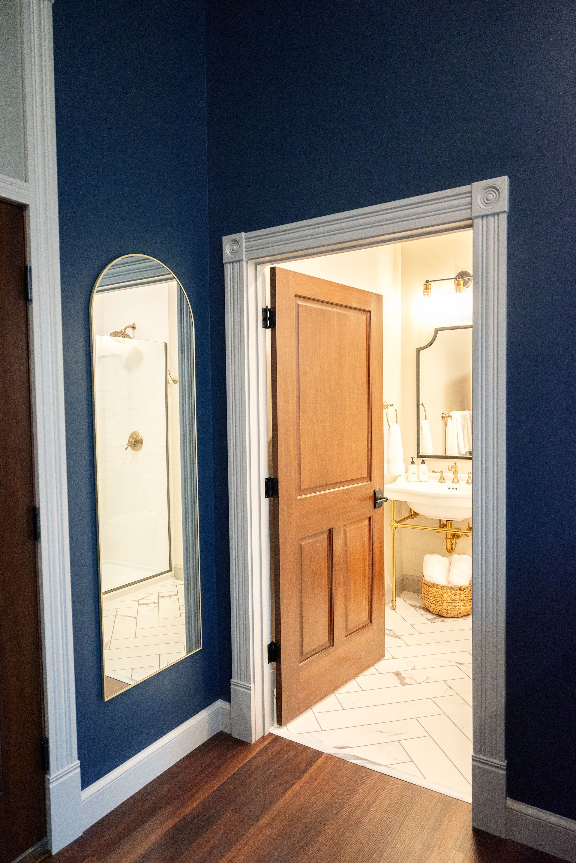 A doorway and arched mirror in a room with blue walls. The open doorway reveals a bathroom.