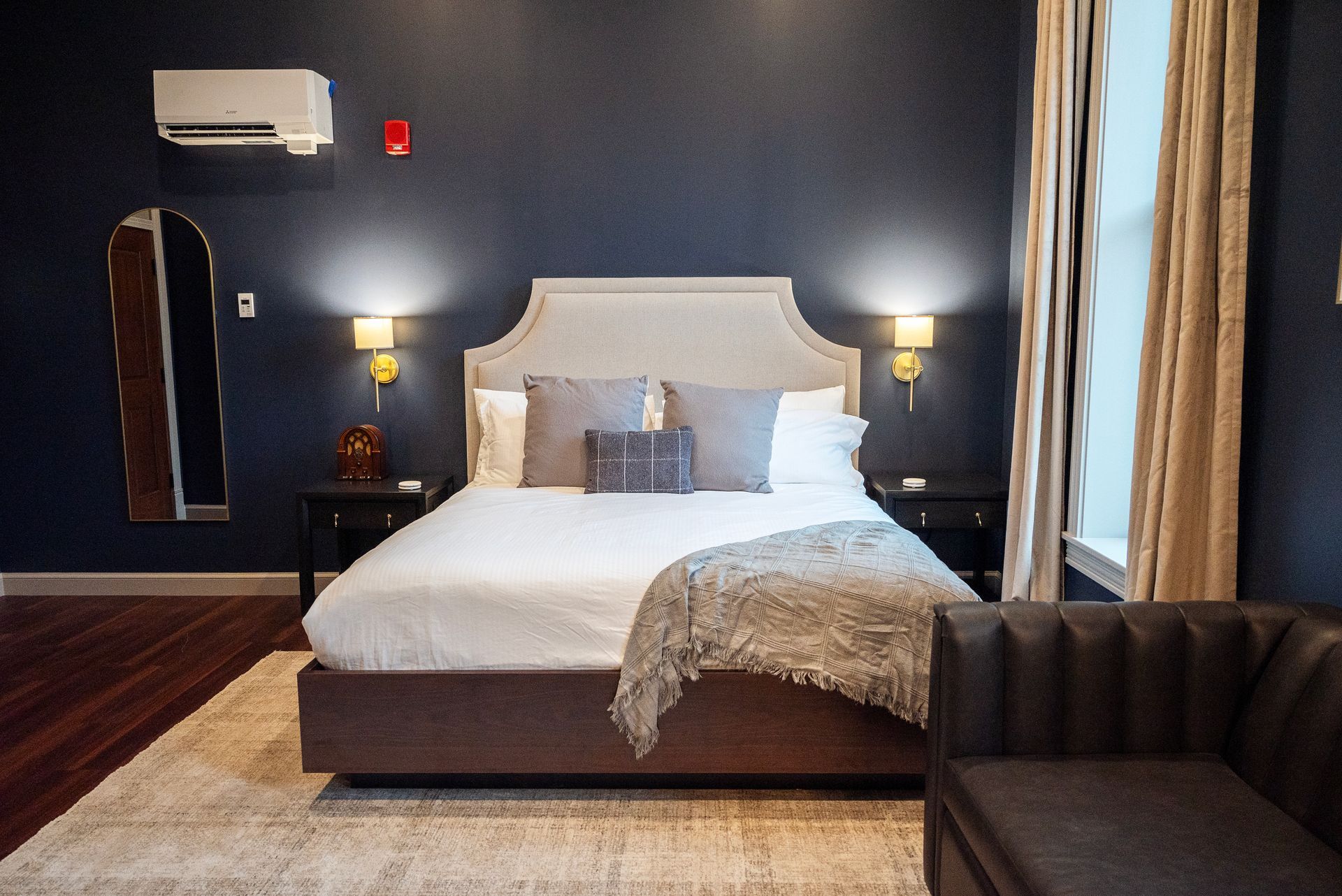 Bedroom with a bed, dark blue wall, dark wood floor, and a small sofa.
