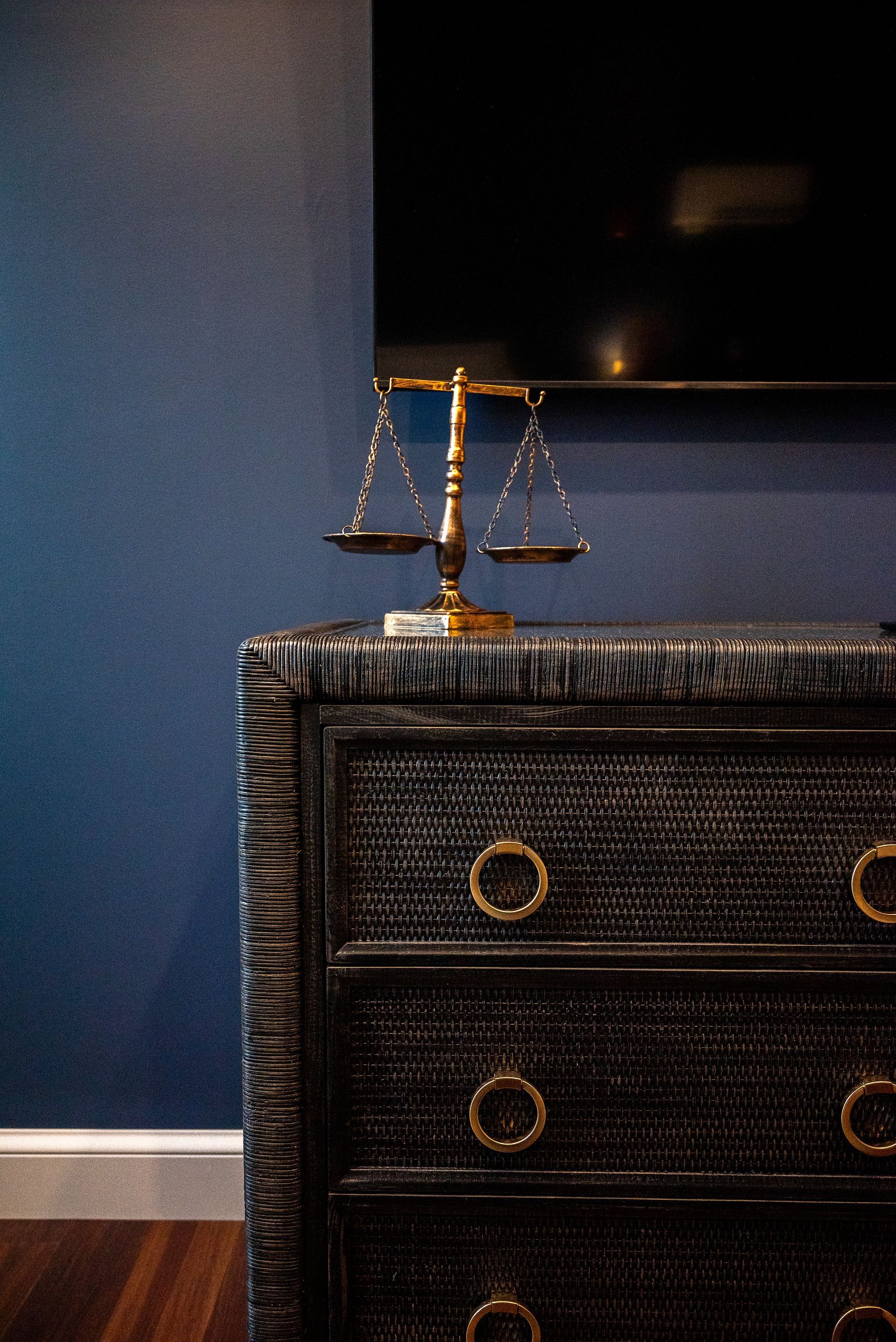 Brass scales on a dark, textured dresser with gold handles, against a blue wall.