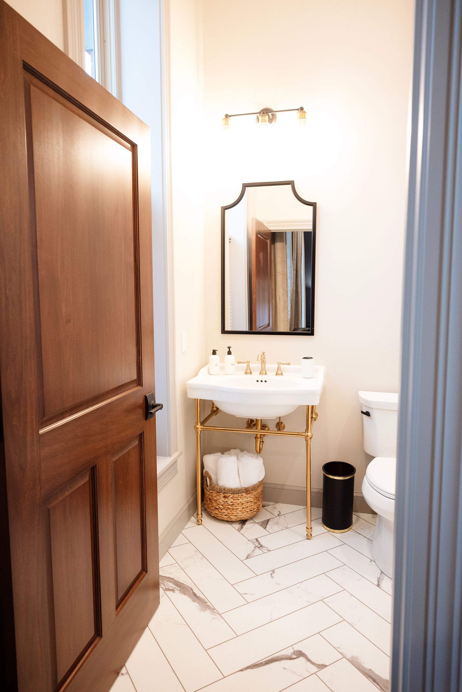 Bathroom with a dark wood door, gold fixtures, and white marble tile.