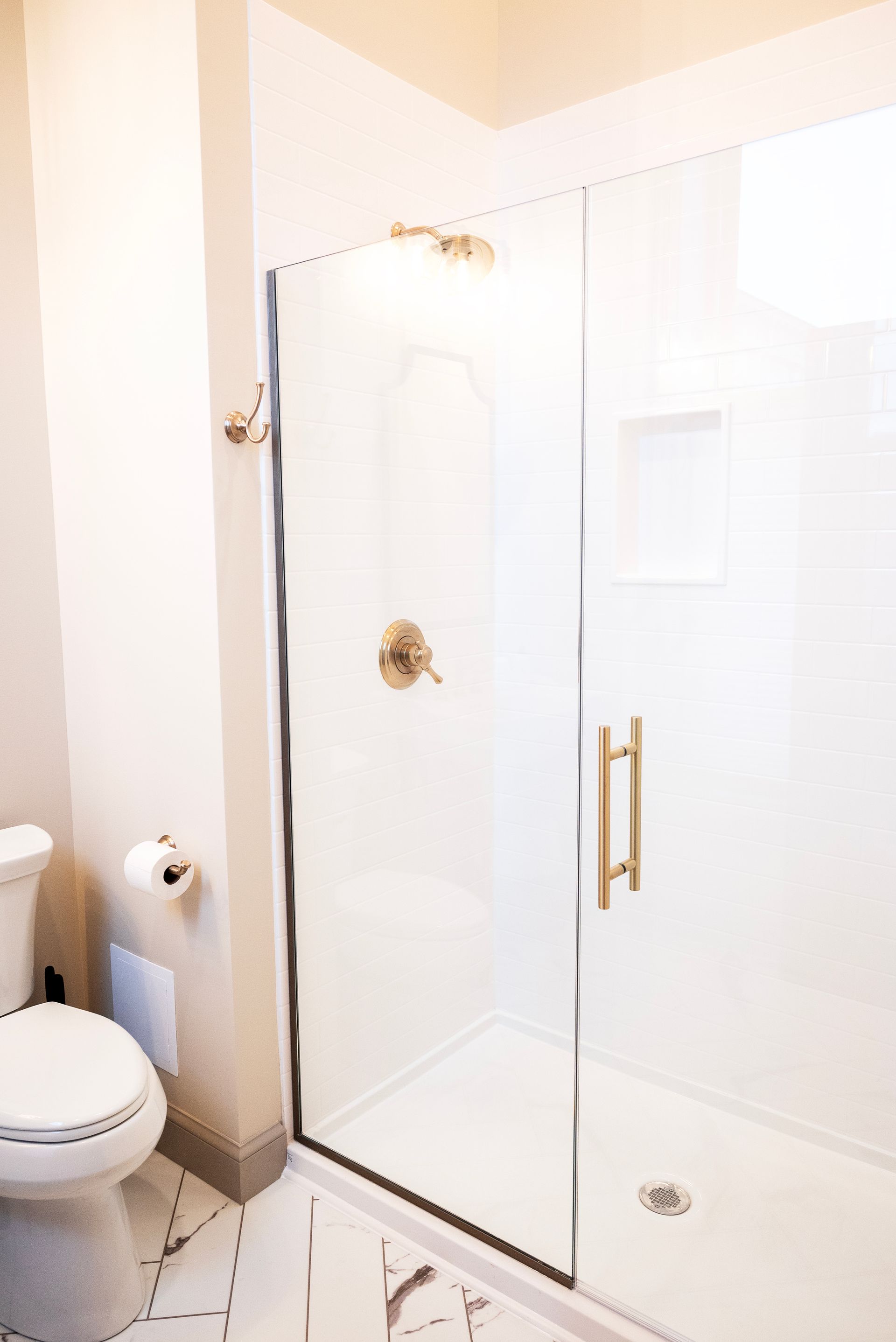 Modern bathroom with glass shower, gold fixtures, white walls, and toilet.