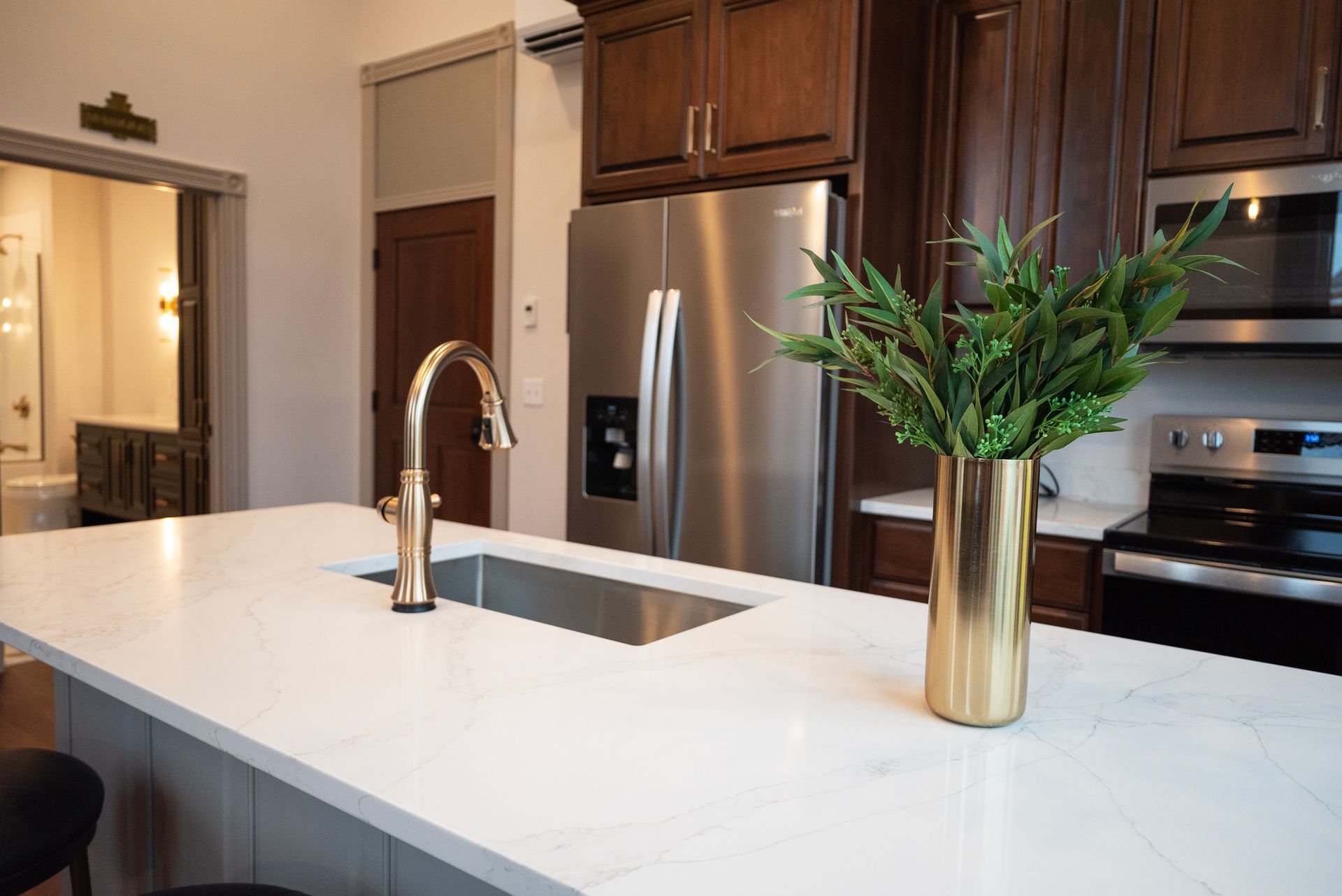 Modern kitchen with gold accents. White countertop island with sink, stainless steel fridge, and greenery in a gold vase.