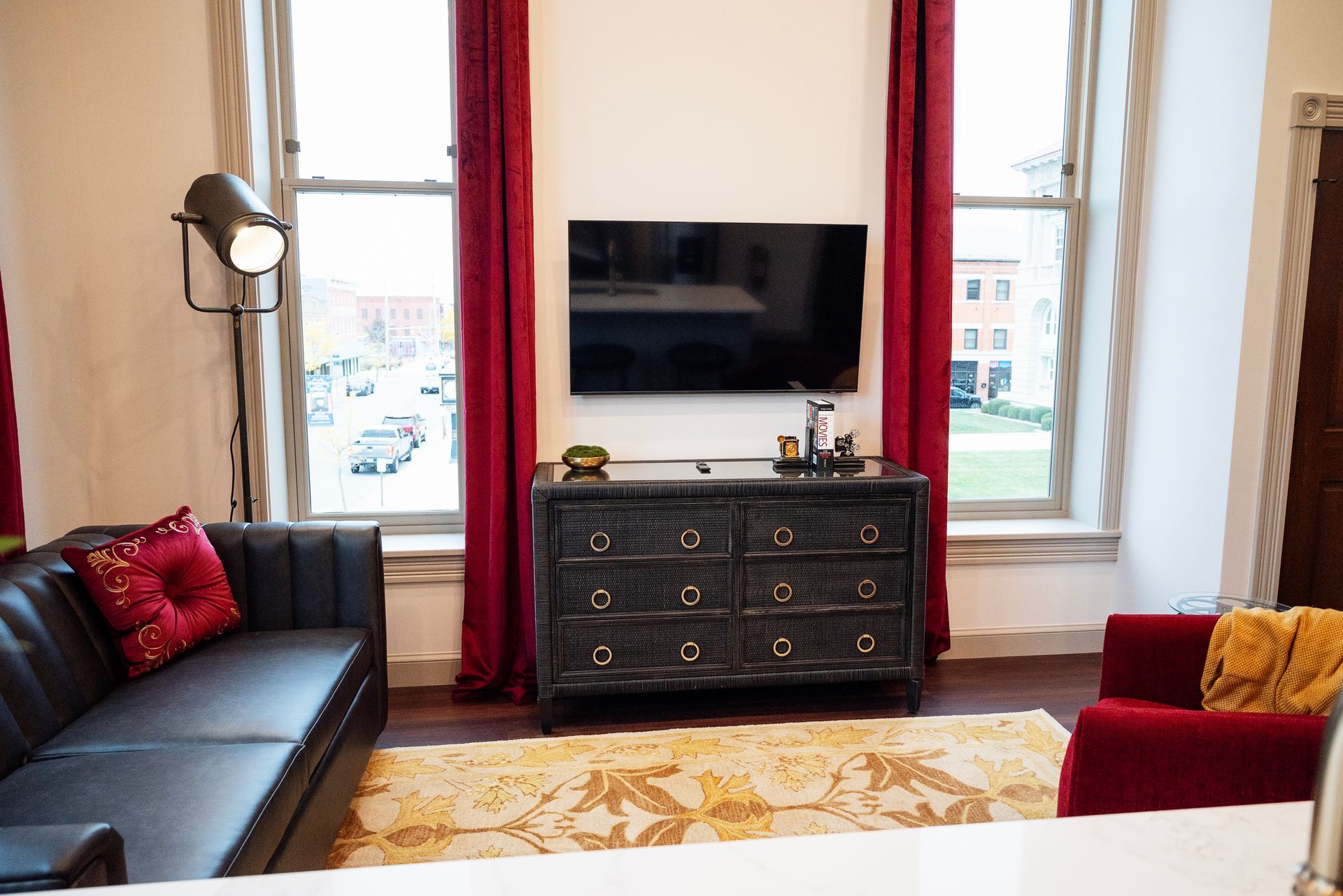 Living room with black sofa, red curtains, and mounted TV above a dark dresser.