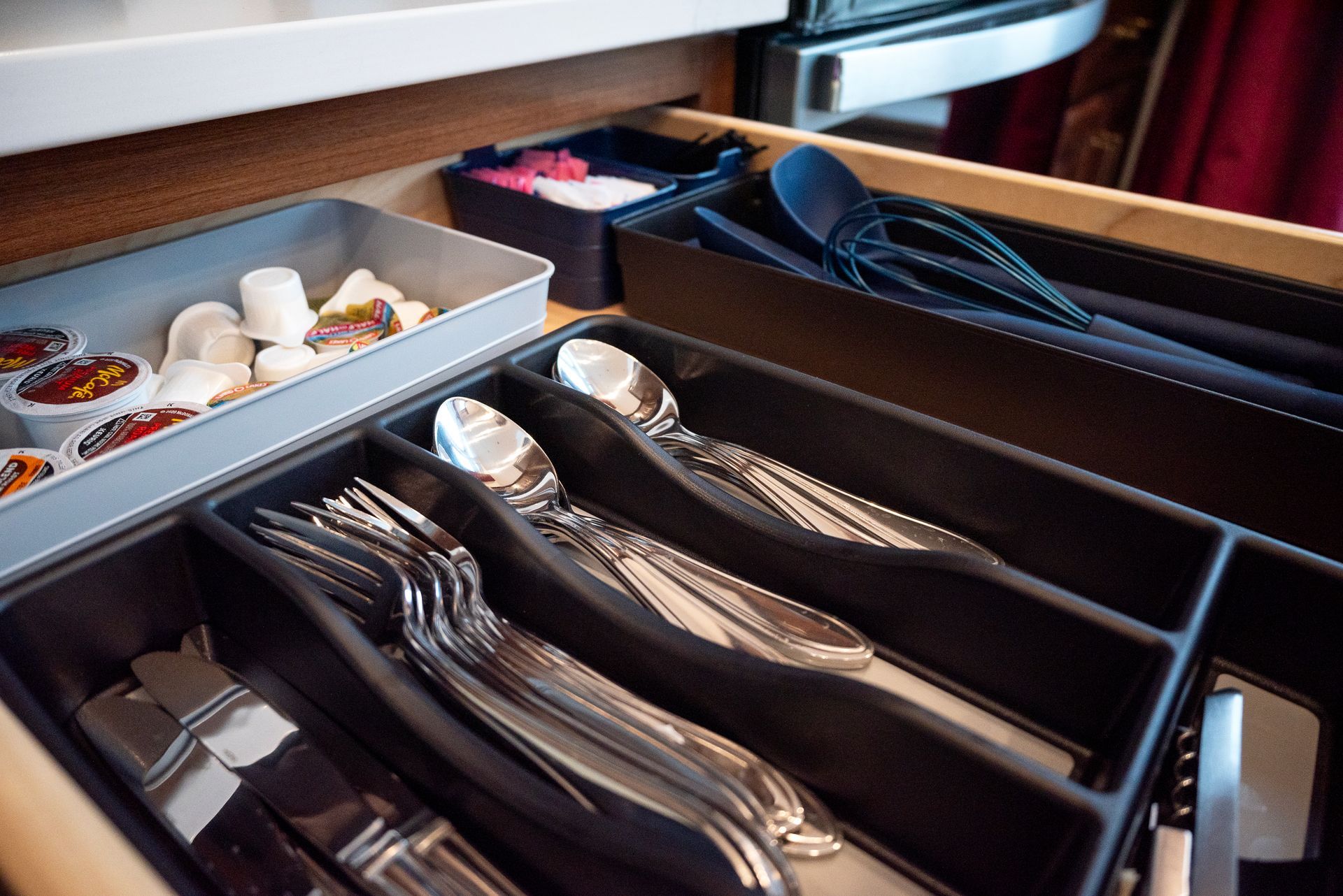 Cutlery drawer with organized silverware, coffee pods, and utensils.