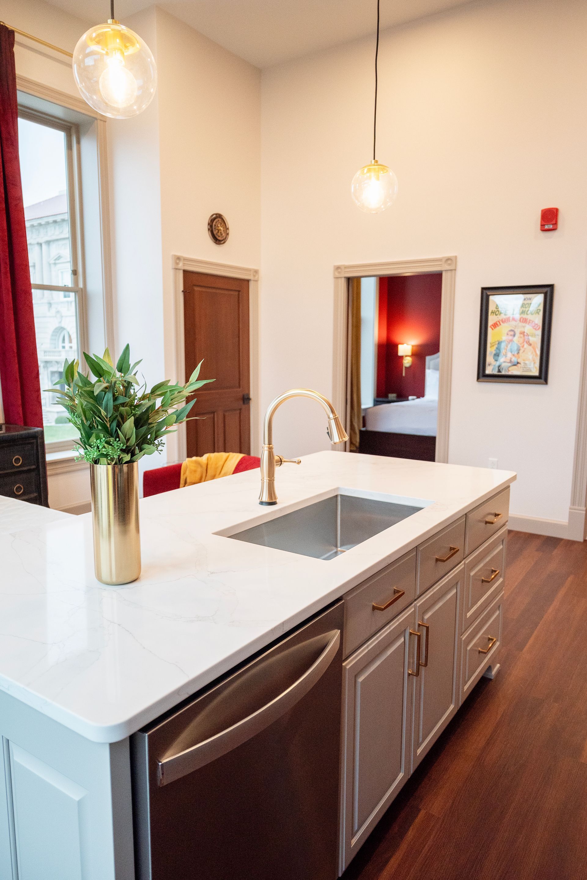 Kitchen with a white countertop island, gold faucet, and view of bedroom with red walls.
